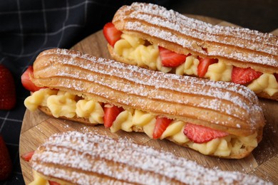 Photo of Delicious eclairs filled with cream and strawberries on table, closeup