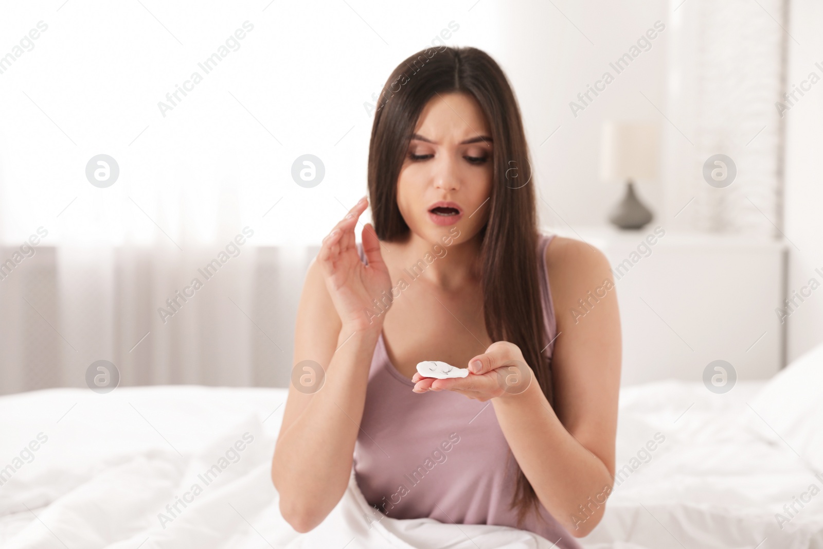 Photo of Beautiful woman holding cotton pad with fallen eyelashes indoors