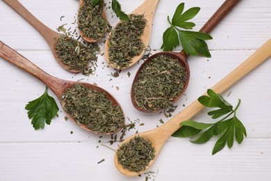 Photo of Spoons with dried aromatic parsley and fresh leaves on white wooden table, flat lay