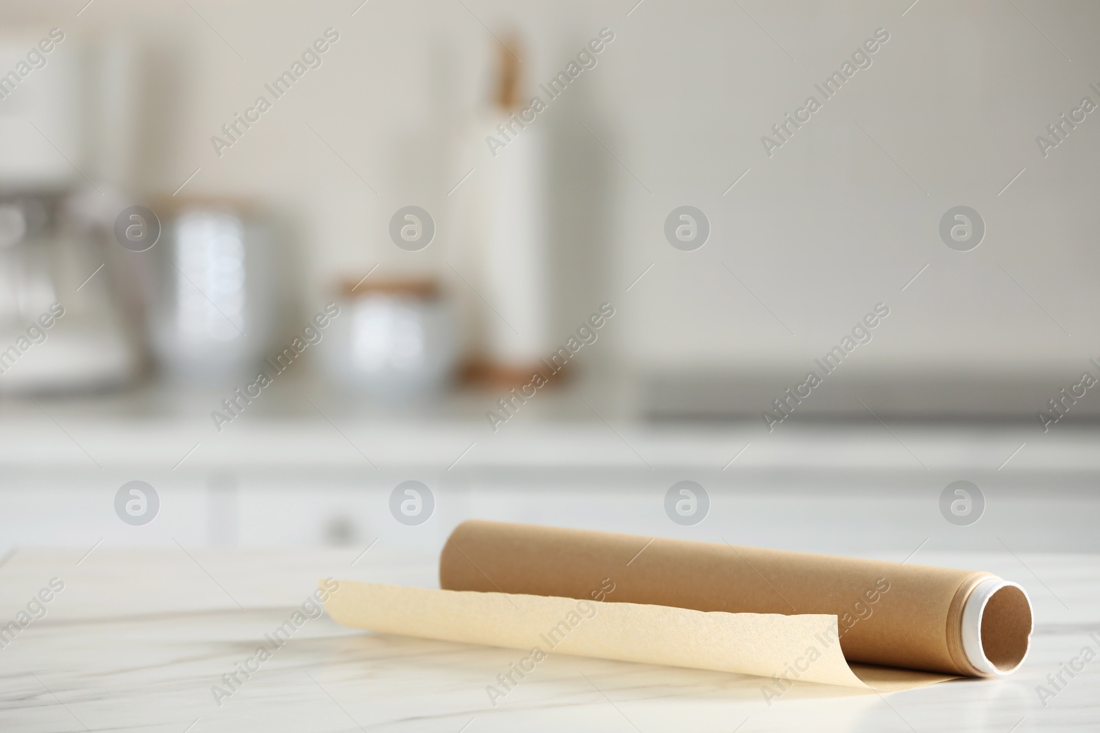 Photo of Roll of baking paper on white marble table against blurred background indoors. Space for text