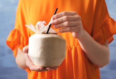 Woman with fresh coconut drink in nut on color background, closeup