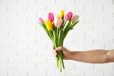 Man holding bouquet of beautiful spring tulips near brick wall, closeup. International Women's Day