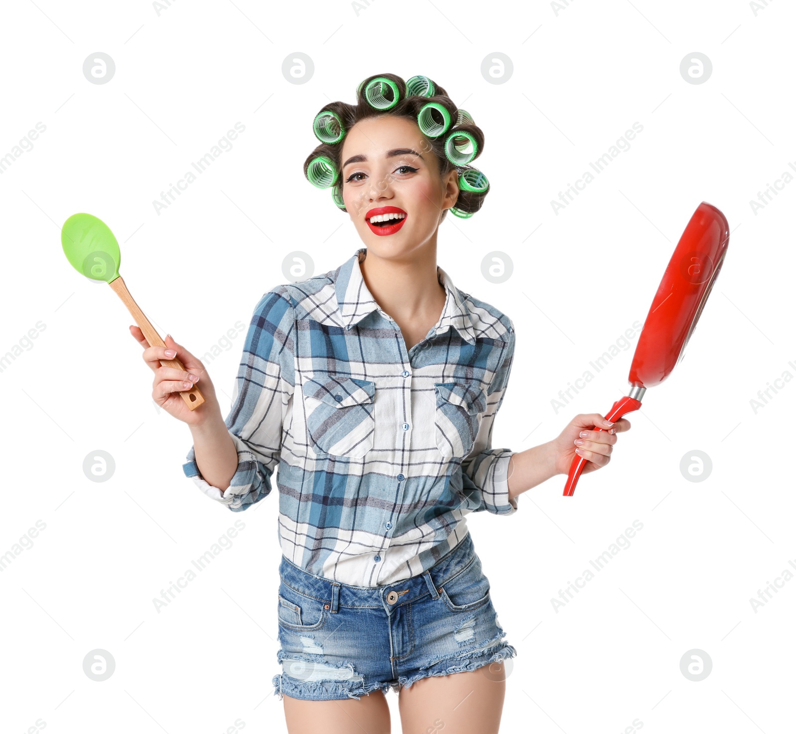 Photo of Funny young housewife with hair rollers holding spoon and frying pan on white background