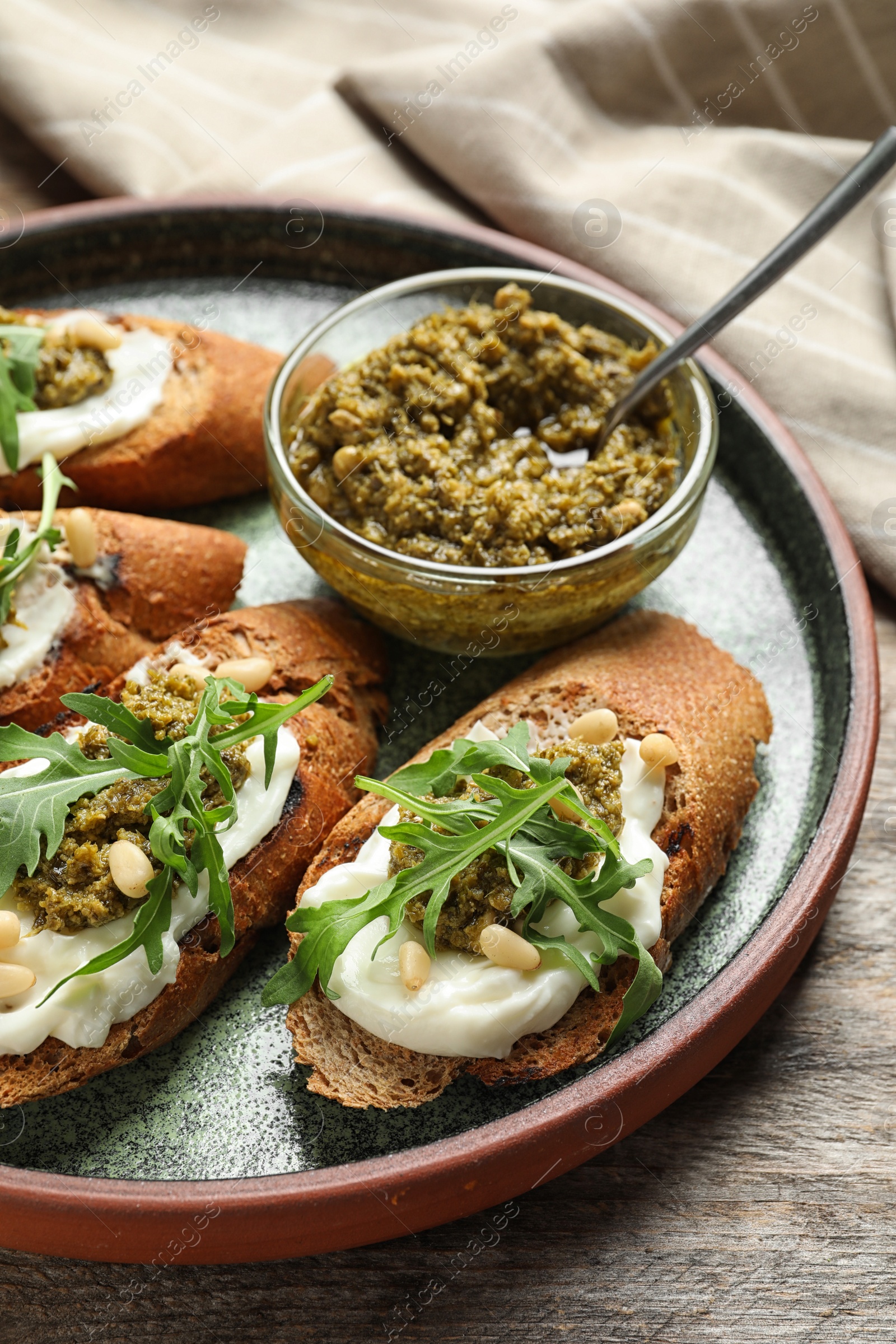 Photo of Plate with tasty bruschettas and pesto sauce on wooden table, closeup