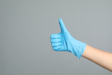 Photo of Doctor in medical gloves showing thumb up on grey background, closeup. Space for text