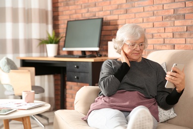 Elderly woman using smartphone on sofa in living room
