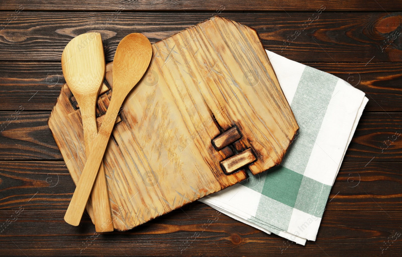 Photo of Board, spatula and spoon with towel on brown wooden table, flat lay. Cooking utensils