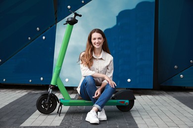 Photo of Happy woman sitting on modern electric kick scooter on city street