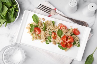 Delicious quinoa salad with tomatoes, beans and spinach leaves served on white marble table, flat lay