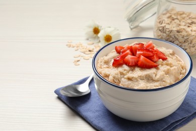 Photo of Tasty oatmeal porridge with strawberries served on white wooden table. Space for text