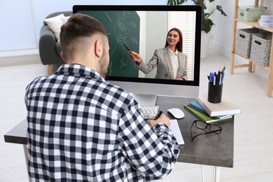 Image of Young man using modern computer at online lesson in room, back view. E-learning