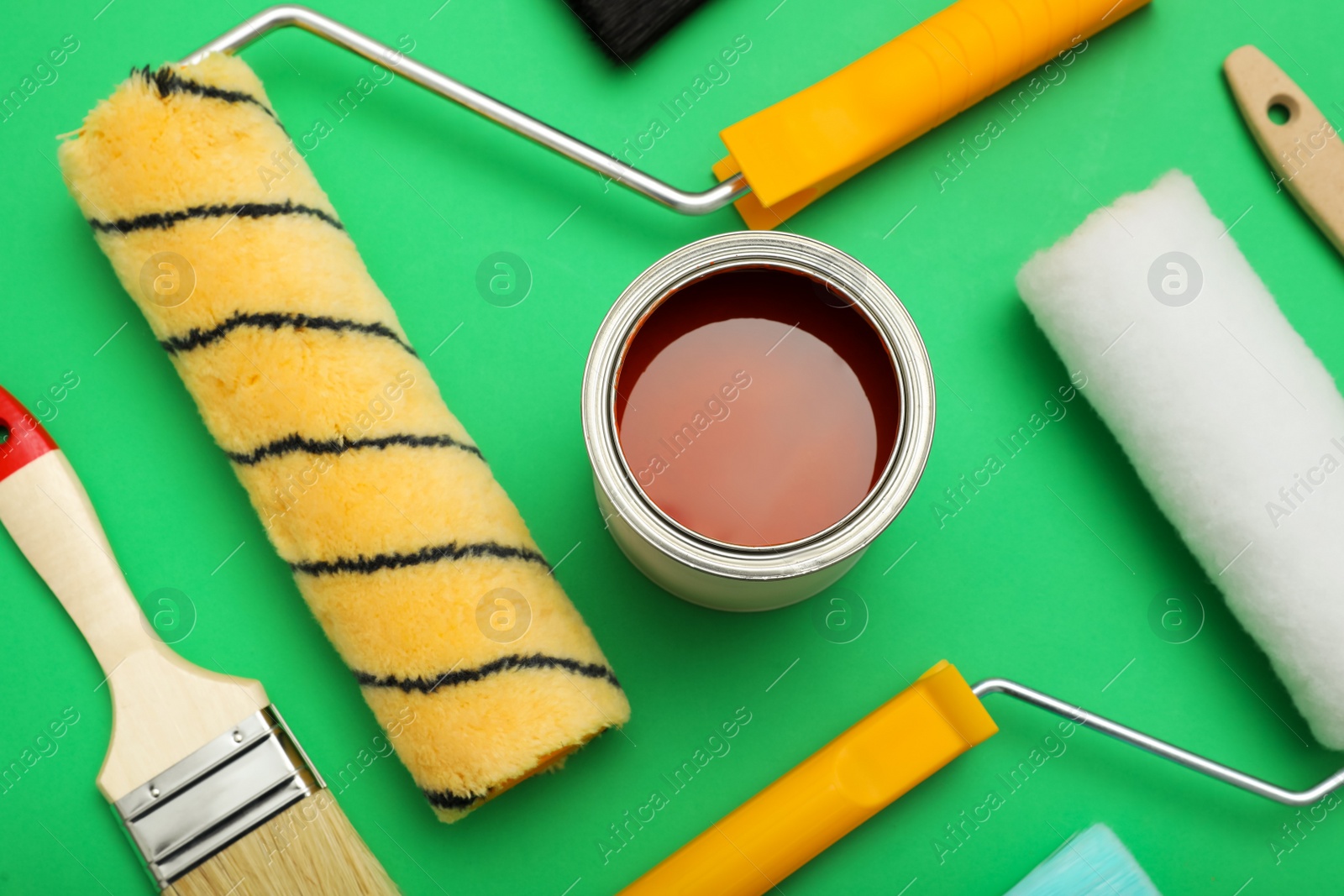 Photo of Can of orange paint, brushes and rollers on green background, flat lay