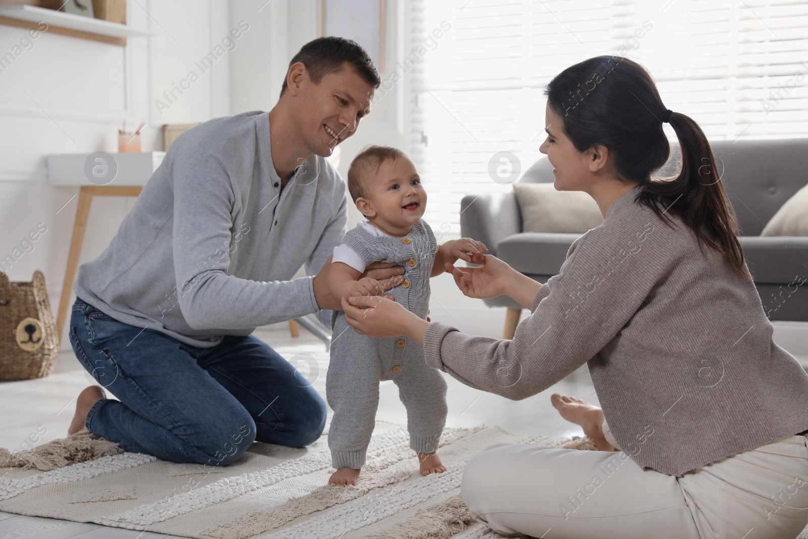 Photo of Parents supporting their baby daughter while she learning to walk at home