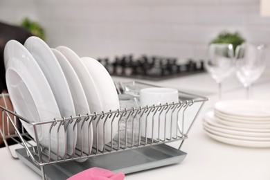 Photo of Dish drainer with clean dinnerware on table in kitchen