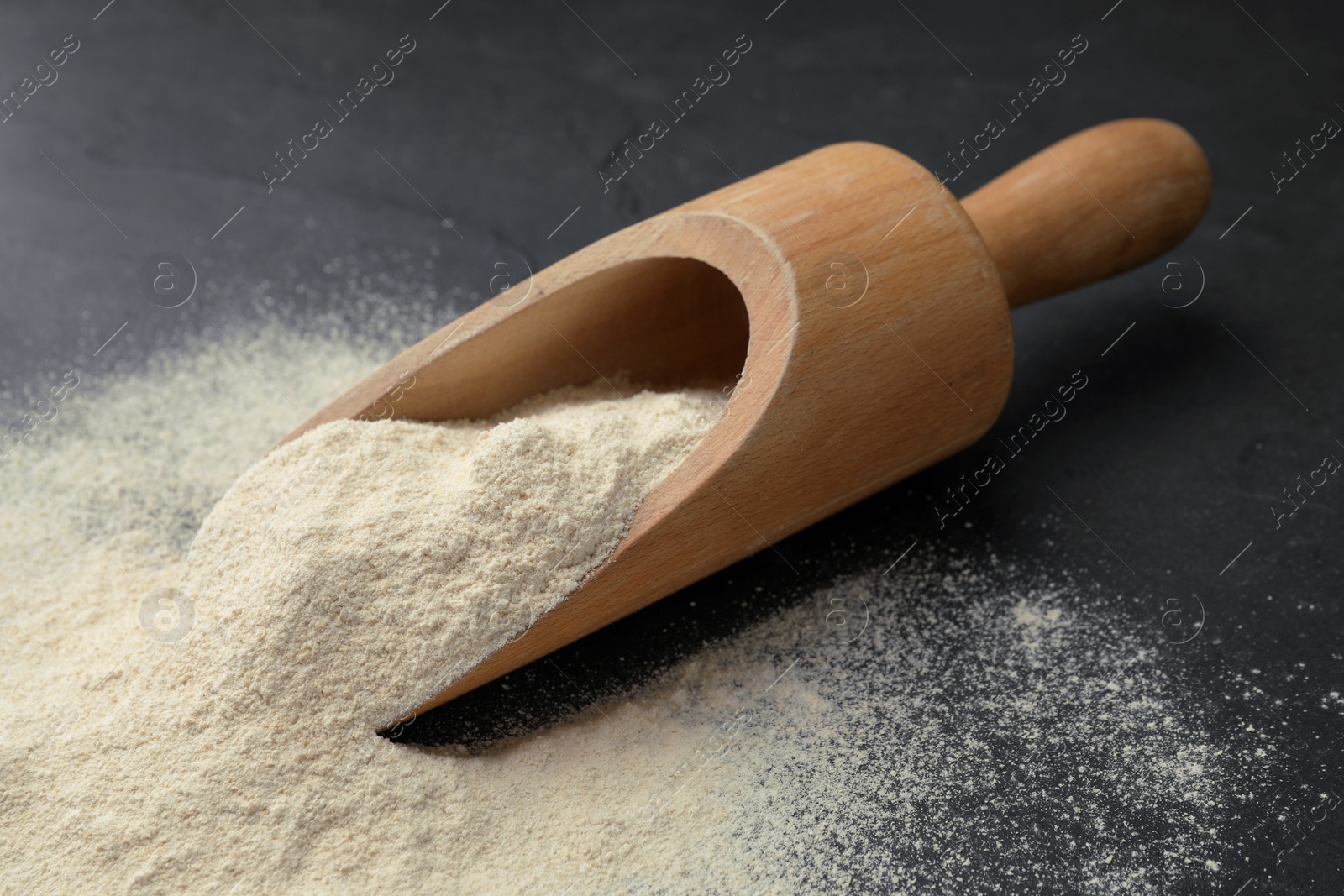 Photo of Wooden scoop with quinoa flour on black table