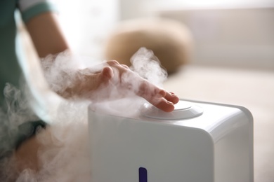 Photo of Woman using modern air humidifier at home, closeup