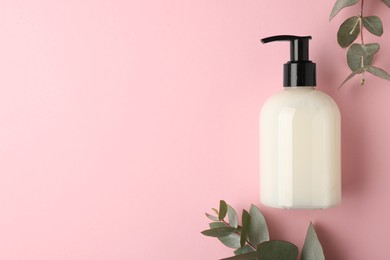 Photo of Bottle of liquid soap and eucalyptus branches on pink background, flat lay. Space for text