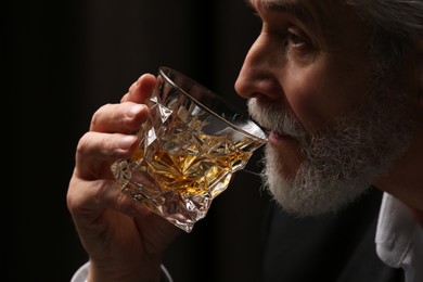 Photo of Senior man in suit drinking whiskey on black background, closeup