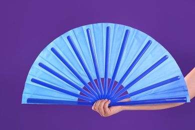Photo of Woman holding blue hand fan on purple background, closeup