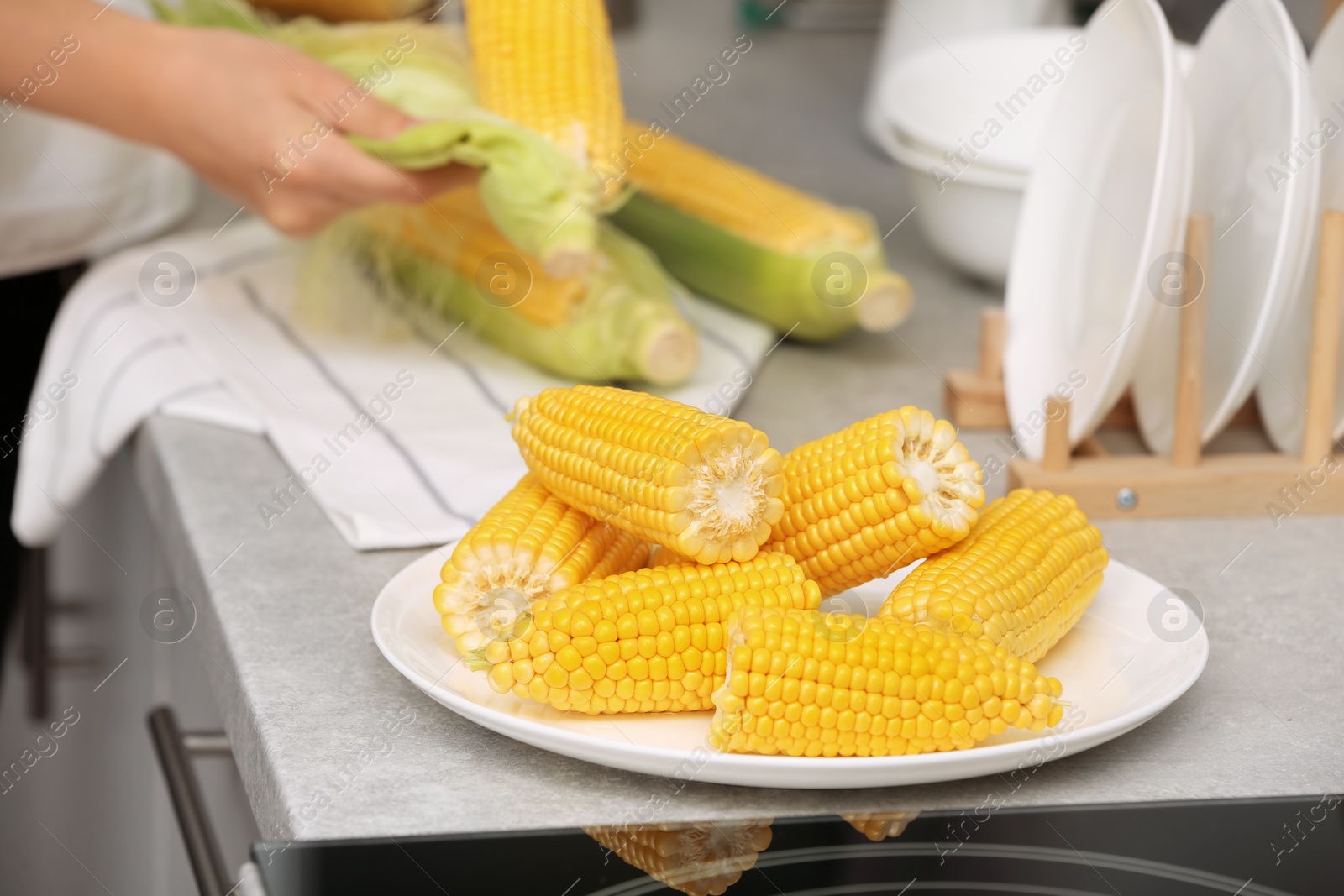 Photo of Plate with ripe corn cobs and blurred woman on background