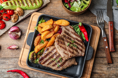 Delicious beef steaks served on wooden table, flat lay
