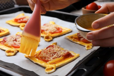 Woman spreading egg yolk onto raw puff pastry with tasty filling, closeup