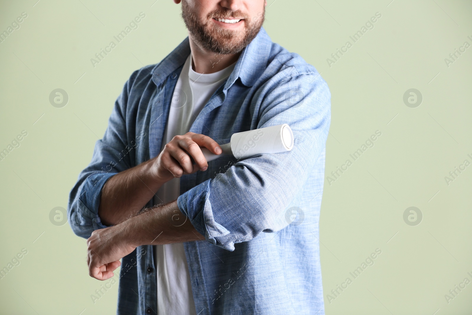 Photo of Man cleaning clothes with lint roller on light background, closeup