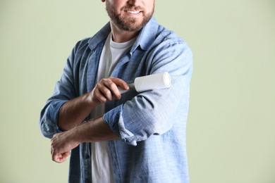 Photo of Man cleaning clothes with lint roller on light background, closeup