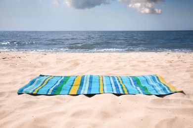Photo of Bright striped beach towel on sandy seashore