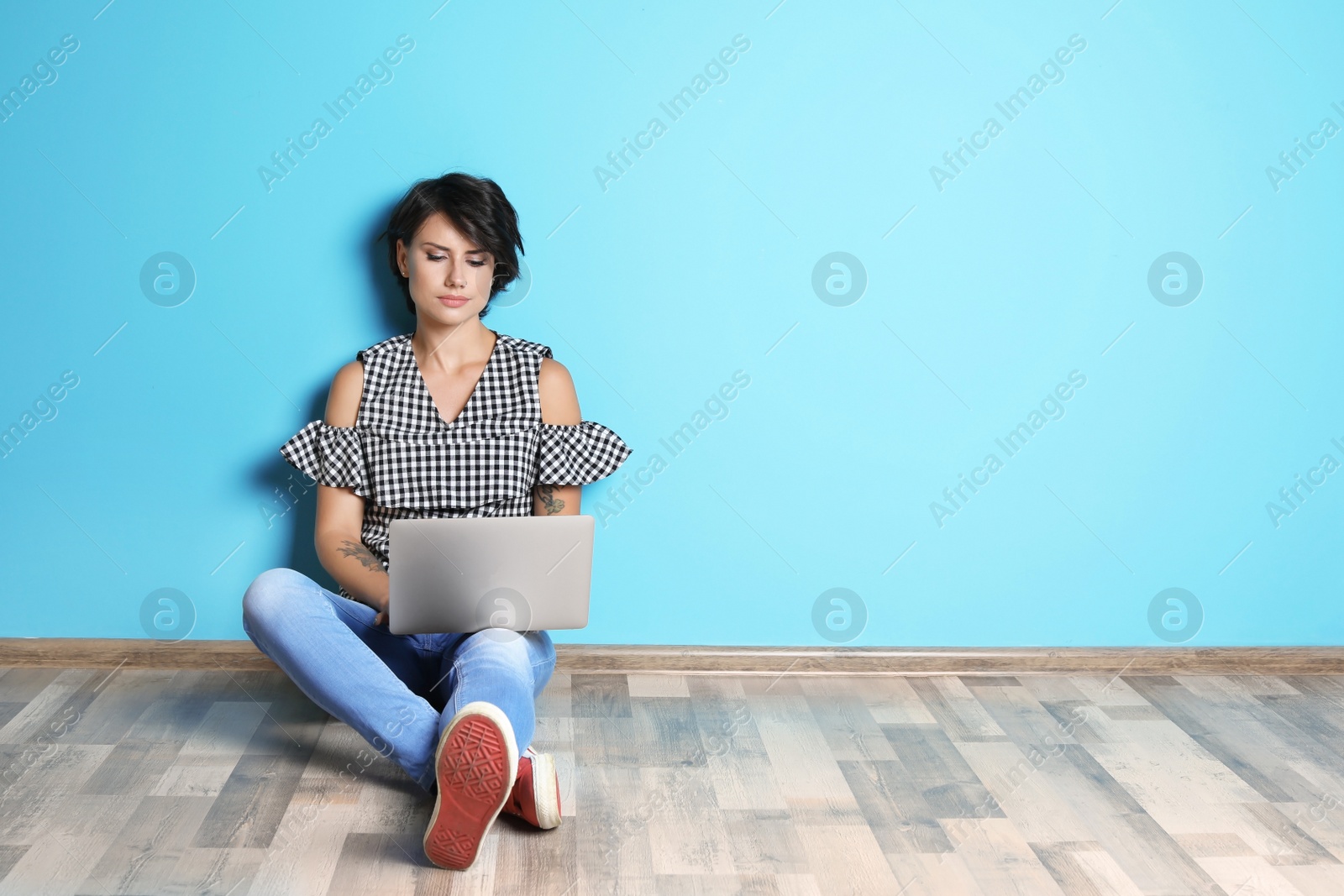 Photo of Young woman with modern laptop sitting on floor near color wall