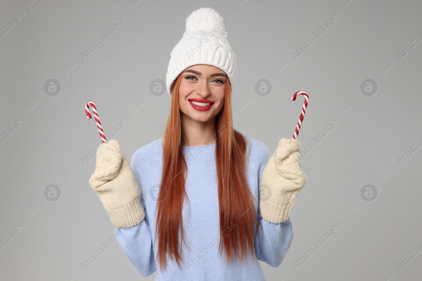 Photo of Young woman in hat and sweater with candy canes on light grey background. Christmas celebration