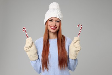 Young woman in hat and sweater with candy canes on light grey background. Christmas celebration