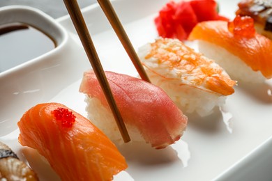 Photo of Taking delicious nigiri sushi with chopsticks on table, closeup