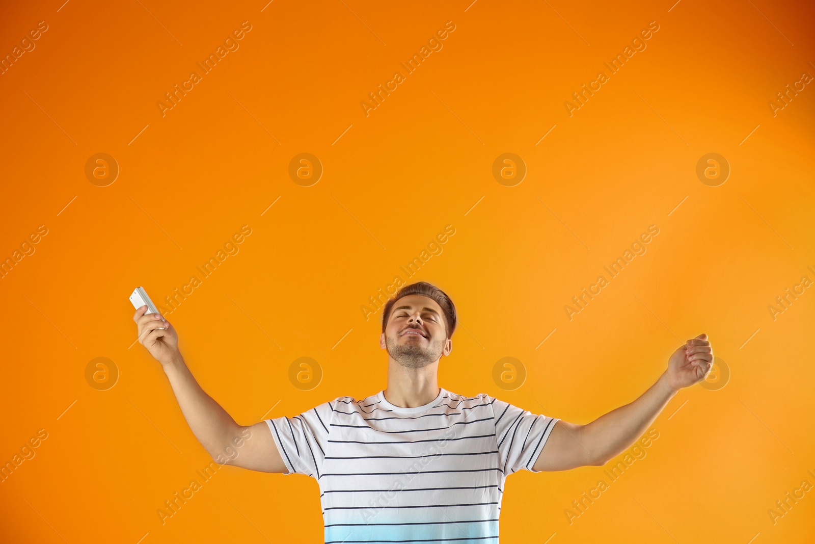 Photo of Happy young man with air conditioner remote on color background