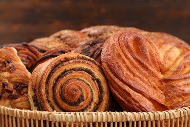 Photo of Wicker basket with different tasty freshly baked pastries on blurred background, closeup