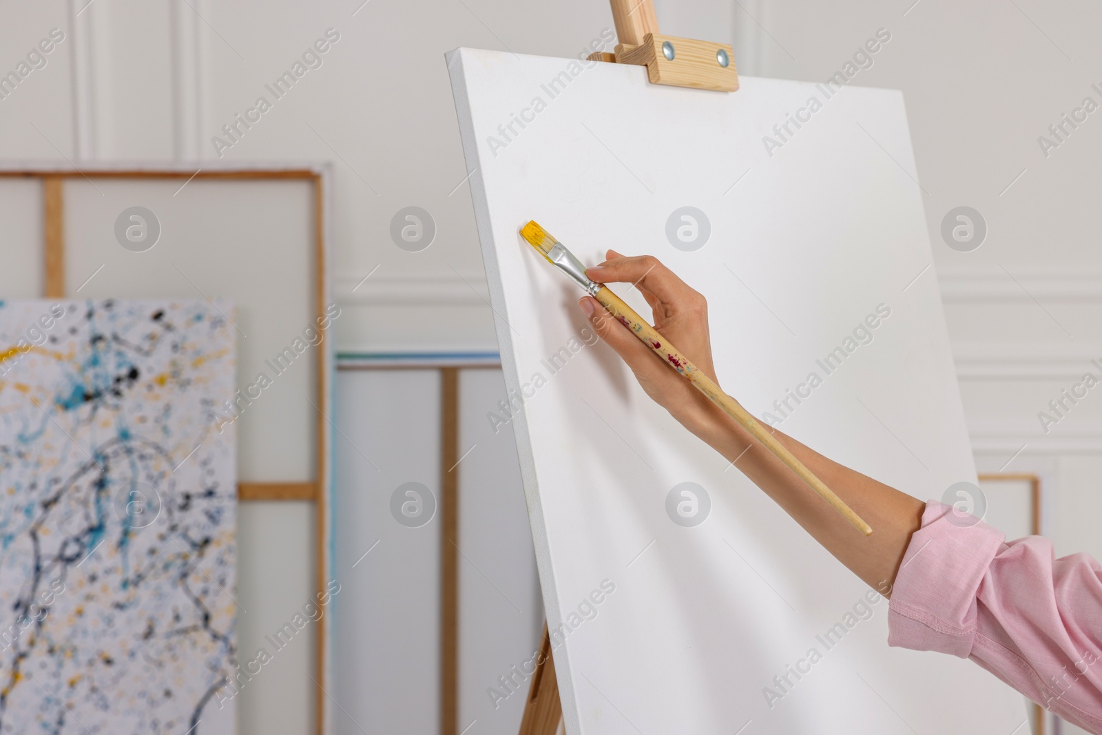 Photo of Woman painting on easel with canvas in studio, closeup