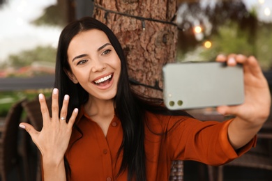 Photo of Happy woman with engagement ring taking selfie in outdoor cafe