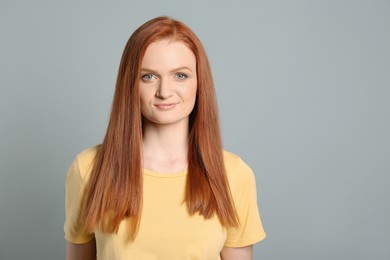Candid portrait of happy young woman with charming smile and gorgeous red hair on light grey background, space for text
