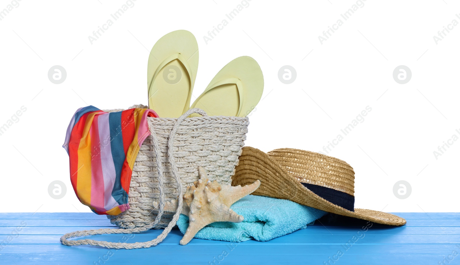 Photo of Stylish bag, starfish and other beach accessories on light blue wooden table against white background