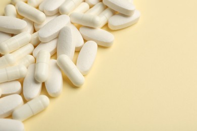 Photo of Vitamin pills on pale yellow background. Space for text