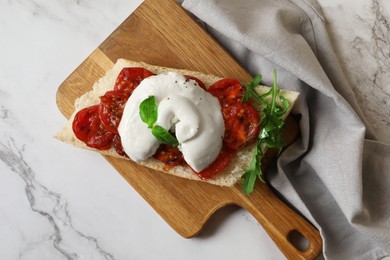 Toast with delicious burrata cheese, tomatoes and arugula on white marble table, top view