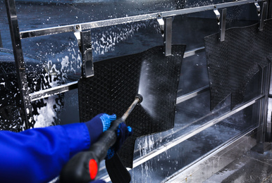 Photo of Worker cleaning automobile floor mat with high pressure water jet at car wash, closeup