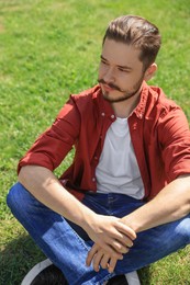 Handsome man sitting on green grass outdoors