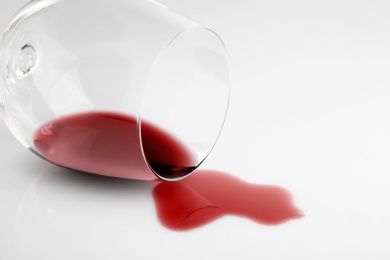 Photo of Transparent glass and spilled exquisite red wine on white background