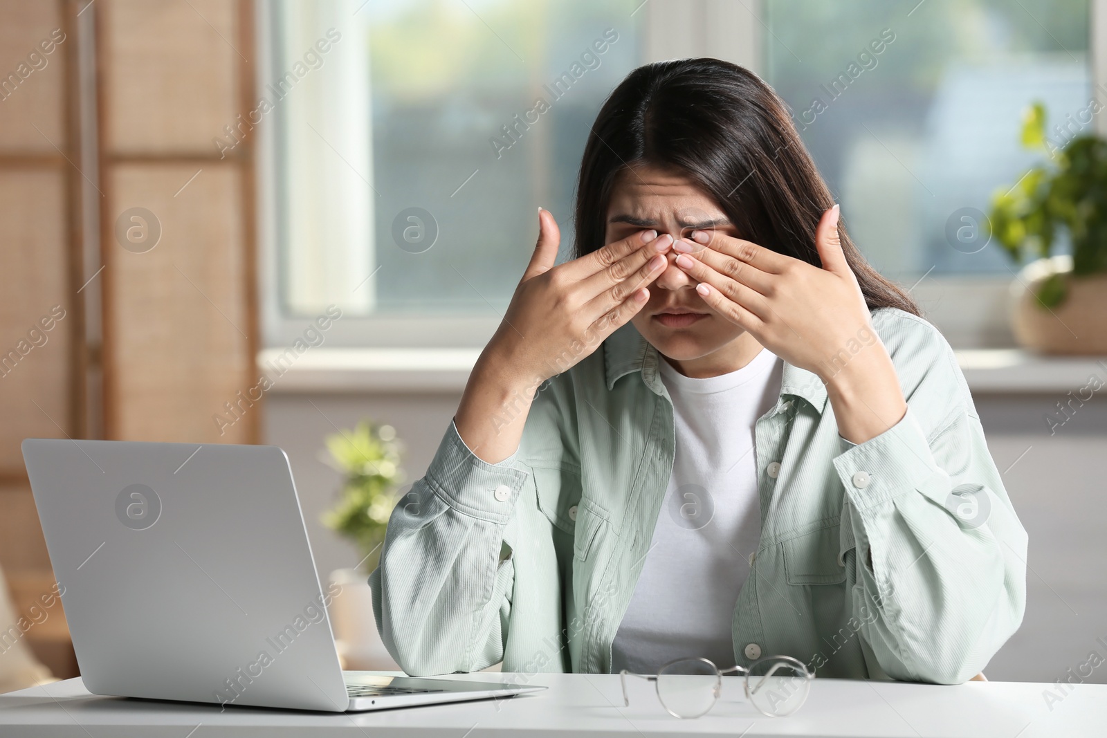 Photo of Young woman suffering from eyestrain at desk in office