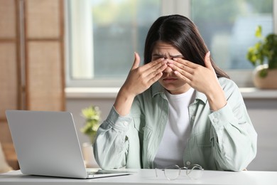 Young woman suffering from eyestrain at desk in office