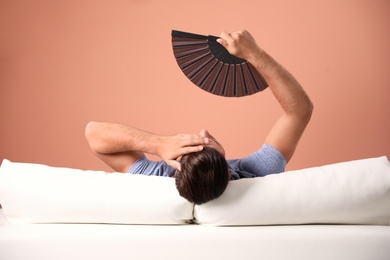 Man with hand fan on sofa. Summer season