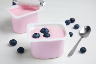 Plastic cup with tasty yogurt and blueberries on white wooden table