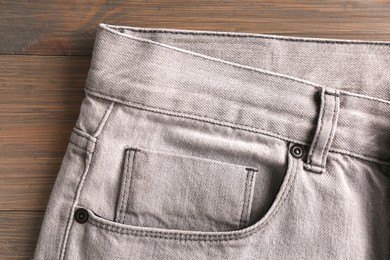 Photo of Stylish light grey jeans on wooden background, closeup of inset pocket