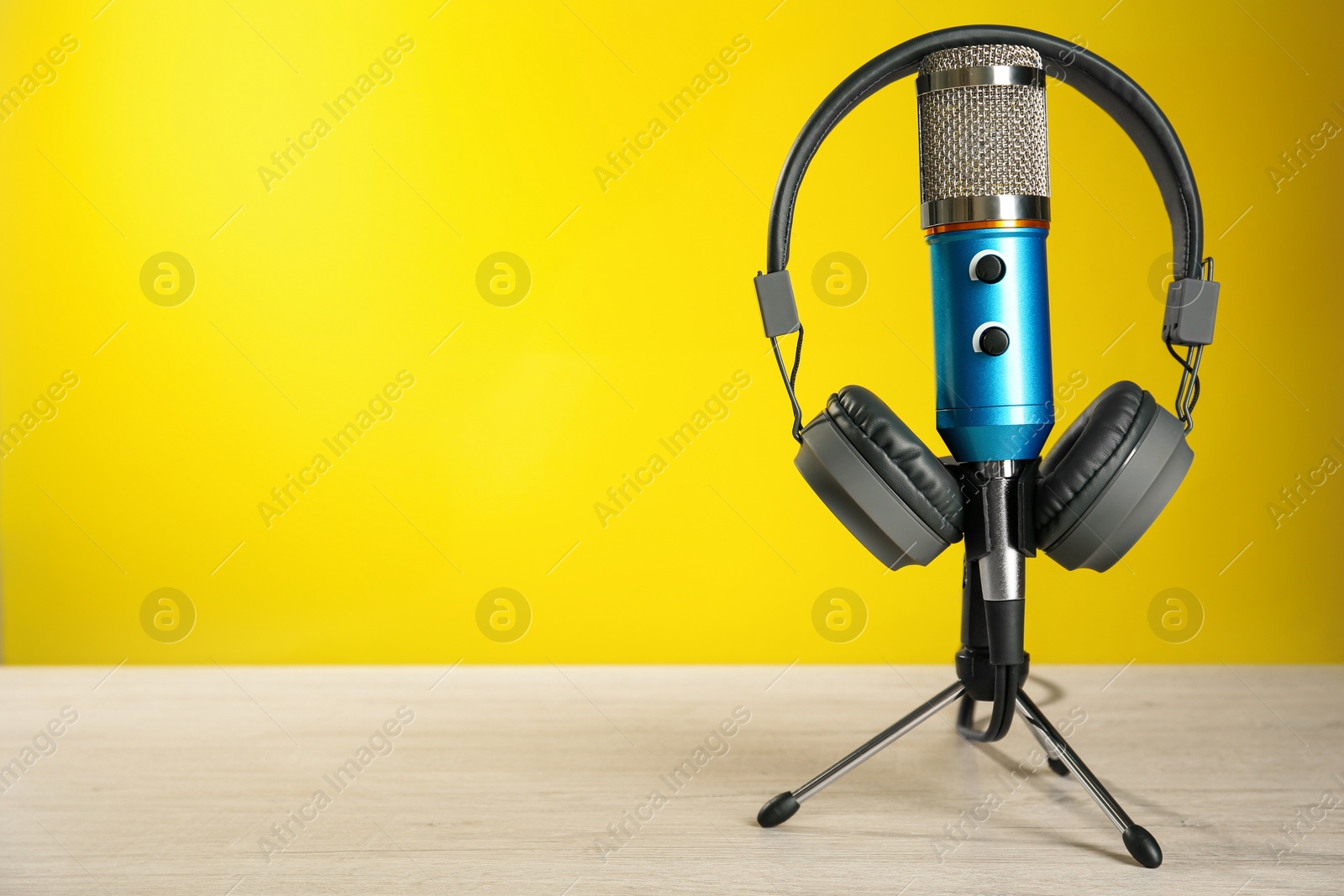 Photo of Microphone and modern headphones on white wooden table against yellow background, space for text